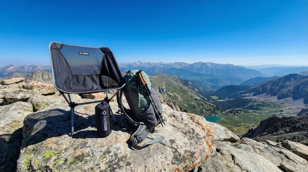 Helinox Chair Zero ultralight backpacking chair set up on a granite summit with a hiker's backpack beside it and panoramic mountain views